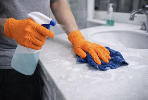 Person using Built Tough 10 Mil Nitrile Gloves With Rock Solid Diamond Grip to clean a countertop with spray and cloth.