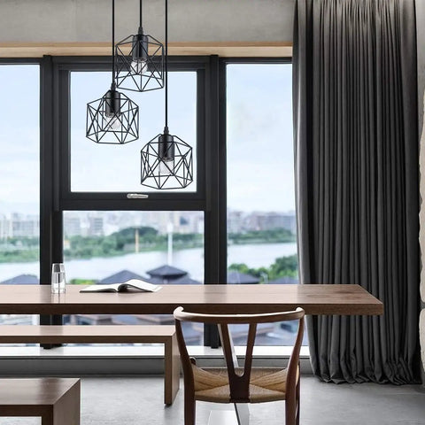 Industrial 3-Light Pendant Light With Black Metal Cage Shade hanging over a modern wooden dining table near a large window.