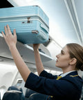 Flight attendant placing 20 Inch Carry On Luggage With Spinner Wheels USB Port Expandable Hard Shell Suitcase in overhead bin.