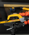 Front view of KATA mini hacksaw for metal, yellow aluminum frame with black handle cutting a metal tube in a vise