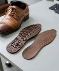 2 Pack Heavy Duty Rubber Sole Replacement Patches For Work Boots And Casual Sneakers on table next to worn brown dress shoe.