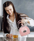 Woman pouring from a pink 2.6 Quart Stainless Steel Whistling Tea Kettle for Stovetop and Induction into a glass cup.