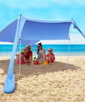 Family enjoying shade under a 7x7 ft portable beach shade tent sun shelter UPF50 canopy with sandbags on a sunny beach day.