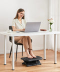 Woman using Adjustable Ergonomic Desk Footrest with Massage under a white desk, promoting posture and leg comfort in home office