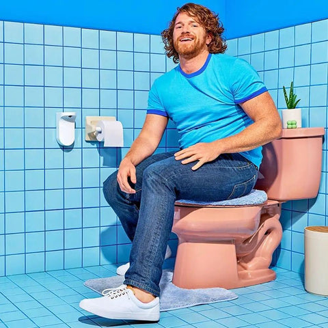 Man using touchless toilet paper foam dispenser kit with wall-mounted setup, next to pink toilet, in a blue tiled bathroom.