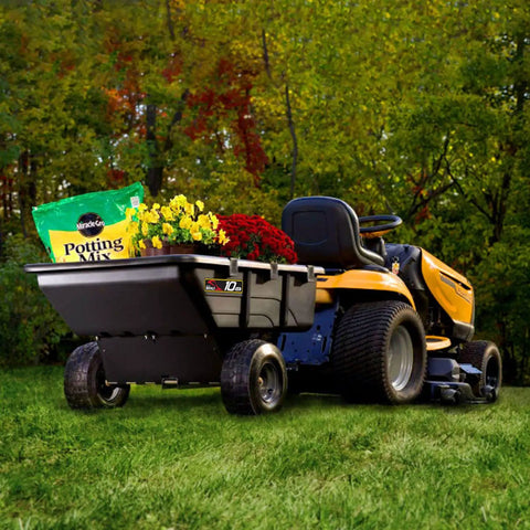 10 Cu Ft Heavy Duty Tow Behind Poly Utility Cart Dump Trailer attached to a yellow mower, carrying potting mix and plants.