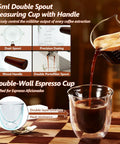 75ml double spout measuring cup with wood handle pouring into double-wall espresso cup for precise brewing, visible features.