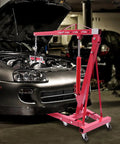 Heavy Duty Folding Hydraulic Engine Hoist Stand Built With Hella Tough Carbon Steel and Zero Sweat Operation For Easy Garage Work and Quick Storage Solutions lifting engine over a car.
