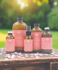 Display of One Ingredient Pure Organic Rose Water Hydrosol Mist in various glass bottles on a wooden table surrounded by petals