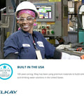 Smiling Elkay factory worker in safety gear, standing in front of machinery. Built in the USA text displayed at the bottom.