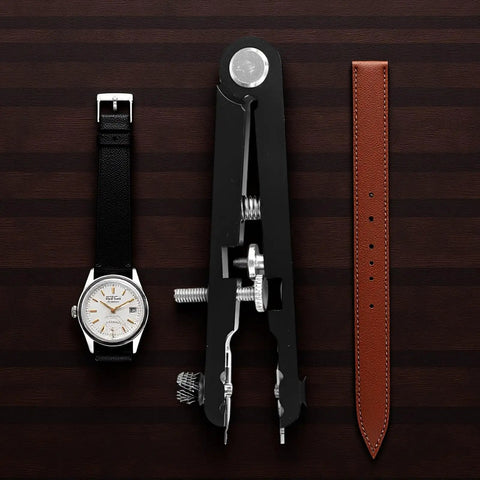 Watch, black Pro Grade Watch Band Removal Tool Kit With 8 Pins, and brown band on wooden background.