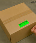 Hand applying Fluorescent Green Inspection Stickers 1 Inch By 2.25 Inch Pack Of 600 For Quality Control Inventory Tracking on box