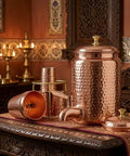 Copper Hammered Water Dispenser Tank With Tap, 6.5 Liter Capacity, Pure Copper Interior, glass set on ornate table