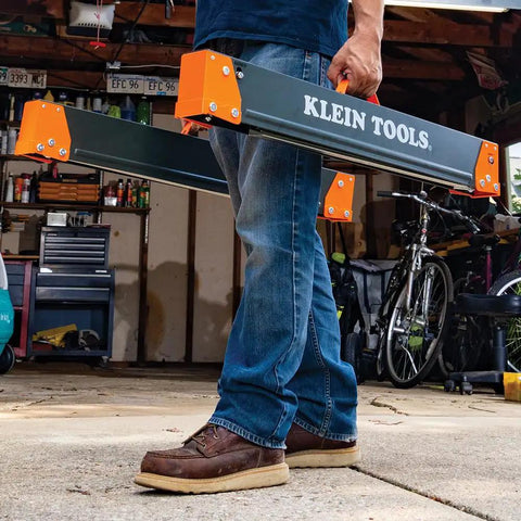 Tough As Nails Folding Sawhorses Heavy Metal Work Platform Non Skid Top Holds A Massive 1300 Lbs Each Rock Solid Rig For Carpenters And Contractors 2 Pack being carried in a garage.