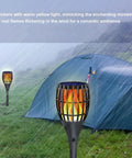 Solar Tiki Torch Lights For Outdoor Spaces With Realistic Flickering Flame Warm Yellow LED Waterproof near a tent in rain.