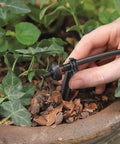 Hand installing No Fuss Drip Watering System With Timer For Containers And Hanging Baskets, Automatic Irrigation For Up To Twenty Plants, Includes Twenty Drippers, Black, in a container garden.