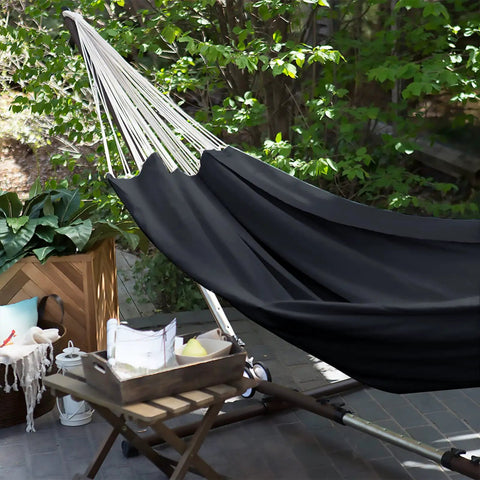 Cotton Portable Camping Hammock With Tree Straps Up To 660 Lbs Travel Bag Indoor Outdoor Patio Backyard Comfort Fabric Hammock For Relaxation All Season Lounging Anywhere in a garden setup, showing black fabric and support straps.