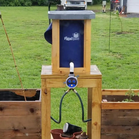 Sprinkler Water Timer For Outdoor Lawn And Garden on a wooden stand with hose connections and control panel, garden in background.