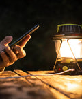 600 Lumen Multi Functional Go To Camping Lantern with USB charging a phone, placed on a wooden surface at night.