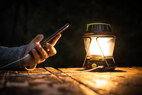 600 Lumen Multi Functional Go To Camping Lantern with USB charging a phone, placed on a wooden surface at night.