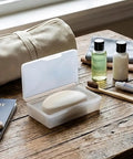 Clear White Travel Soap Box with Lid for On The Go Organization on a wooden table with travel items