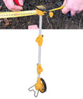 Keenso Digital Display Measuring Wheel Accurate Professional Distance with a yellow handle and measuring tape on soil.