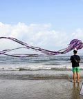 Person flying Octopus Kite For All Ages Large Frameless Soft Parafoil With Long Tail Easy To Fly For Adults And Kids at the beach.