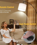 Woman using remote for arc floor lamp with foot switch, 81-inch tall dimmable LED standing light in living room.