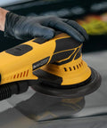 Kickin Up Dust Free Surfaces With This Beefy Electric Random Orbital Sander That Features Shop Vac Hookup Plug In Cord And Sharp Ceramic Discs For Tight Woodworking Jobs with a close-up of a user's hand on the tool.