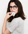 Eyeglass lens wipes packet held by woman with black-framed glasses (front view)