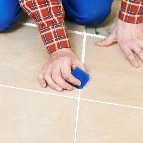 Person using Two Piece Caulking Tool Set For Sealant, Grout, And Caulk Smoothing, Flexible Plastic Tools With 10 Edge Shapes For Kitchen, Bathroom, And Floor Use, Blue on floor tiles.