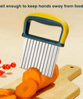 Crinkle cutter knife with yellow and teal handle and stainless steel blade cutting carrot slices on wood cutting board.