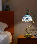 Sea Blue Dragonfly Handmade Stained Glass Desk Lamp with Metal Leaf Base beside bed in dimly lit room