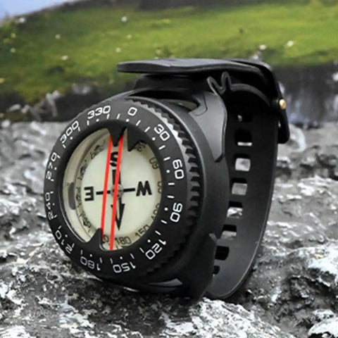 All Weather Dive Compass With Built In Light For Clear Readings Anywhere Waterproof Survival Tool shown on rocky terrain.