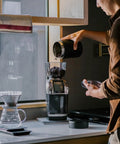 Heavy Duty Commercial Coffee Grinder Featuring Flat Steel Burrs And 260 Grind Settings For Espresso And Pour Over Brewing with coffee beans being poured.