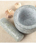 Heavy Duty Granite Mortar And Pestle Set With Anti Slip Base For Grinding Spices Herbs Garlic Pepper Nuts Coffee Beans And More Pro Grade Guacamole And Salad Prep Non Porous Easy To Clean And Durable Kitchen Tool on a kitchen counter with garlic cloves