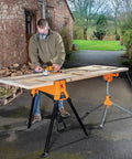Person using Beefed Up Heavy Duty Portable Clamping Jawhorse With Foot Pedal For Hands Free Operation Folding Workbench Tripod Table 2200lb Capacity Ideal For Woodworking Repairs And Construction outdoors.
