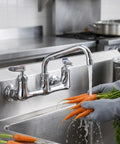 Lead-Free 8" Center Wall Mount Commercial Kitchen Faucet - 8" Swivel Spout washing fresh carrots in a stainless steel sink.