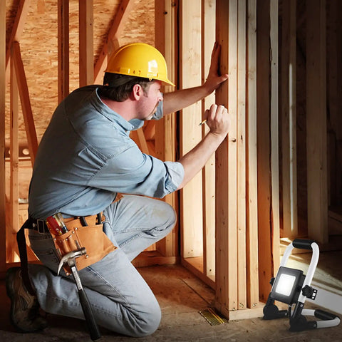 Worker using 3000 Lumen LED Work Light With Adjustable Stand And Switch on job site, illuminating wooden frame construction area.