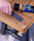 All Purpose Latex Wood Filler In Walnut, 6 Oz being applied to a wooden table corner with a putty knife, enhancing interior and exterior wood surfaces.