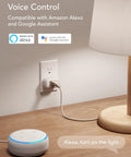 Voice-controlled mini smart plug with Alexa next to a lamp on a desk, demonstrating 2.4GHz WiFi compatibility.