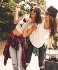 Two women with luggage outdoors, smiling and enjoying a sunny day, dressed in casual jeans and hats.