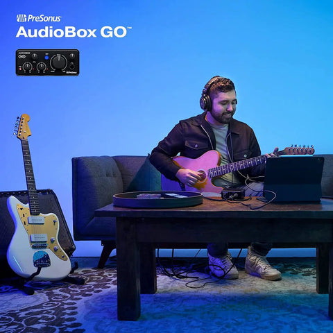 Man playing guitar with Ultra Compact USB C 2x2 Audio Interface Bundle, headphones, on light blue room setup.