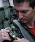 Person attaching Sidewinder 47 Lumen Compact II Rescue Flashlight With Rail Mount And Headstrap to MOLLE vest in Coyote Packaging.