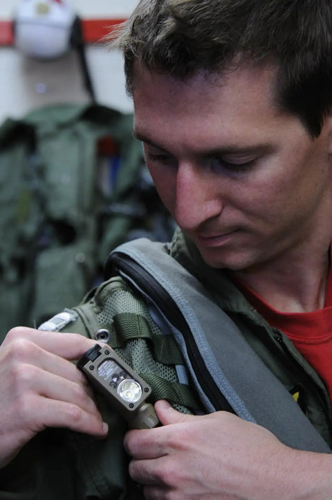Person attaching Sidewinder 47 Lumen Compact II Rescue Flashlight With Rail Mount And Headstrap to MOLLE vest in Coyote Packaging.