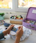 Close-up of a person embroidering at a craft station with threads and a mannequin, no Bronze Floor Magnifier Lamp With 8x10 Inch Shade visible.