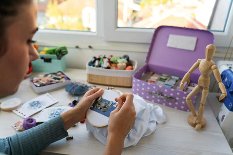 Close-up of a person embroidering at a craft station with threads and a mannequin, no Bronze Floor Magnifier Lamp With 8x10 Inch Shade visible.
