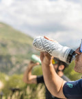 Rock Solid Double Wall Insulated Cycling Water Bottle Keeps Drinks Ice Cold On Long Rides Optimized Bike Cage Fit With Hassle Free Perforated Squeeze Valve For Rapid Sipping During Intense Grinds In Classic Navy held by cyclist during outdoor ride.