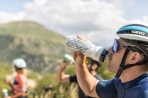 Rock Solid Double Wall Insulated Cycling Water Bottle Keeps Drinks Ice Cold On Long Rides Optimized Bike Cage Fit With Hassle Free Perforated Squeeze Valve For Rapid Sipping During Intense Grinds In Classic Navy held by cyclist during outdoor ride.