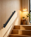 Badass Black Stainless Steel Wall Mount Handrail For Stairs And Hallways With Heavy Duty Support and Tight Secure Grip For Indoor Renovation And Exterior Installations mounted on a wooden wall.